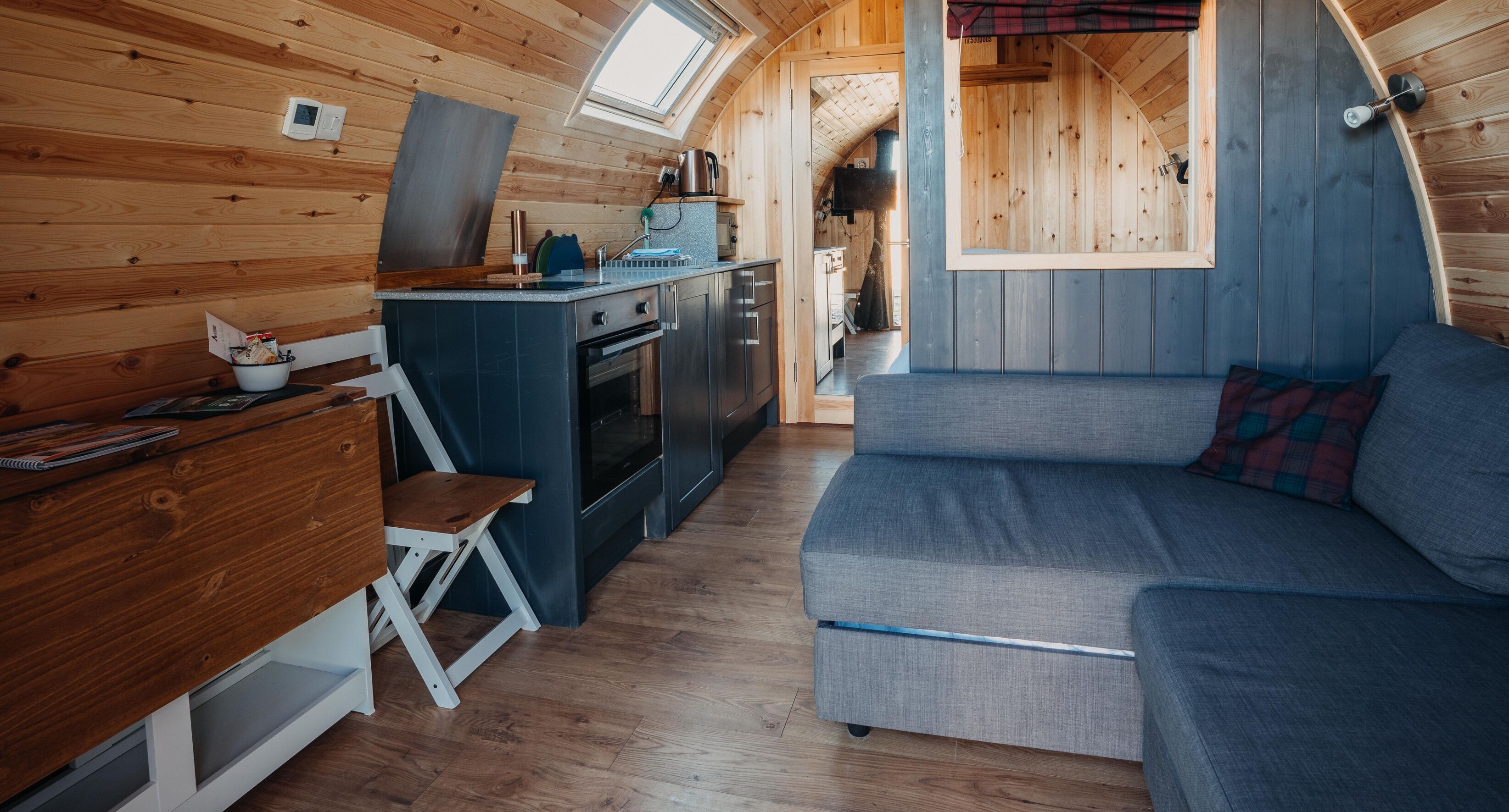 Une cuisine compacte dotée d’un four encastré, un petit coin repas avec une table et une chaise en bois, et un coin salon confortable avec un canapé.