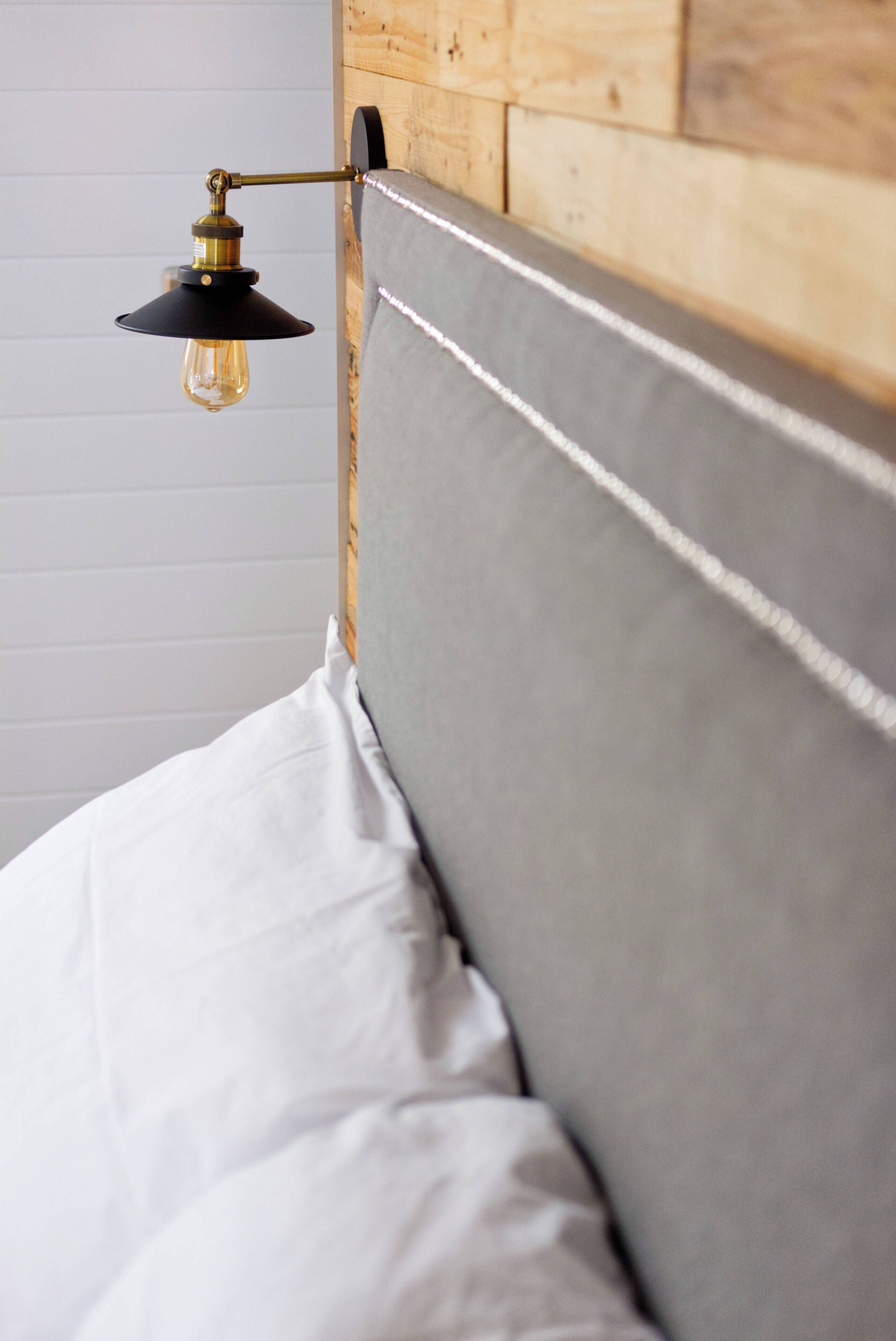 Una cama con cabecera tapizada en gris, lámpara colgante y ropa de cama blanca.