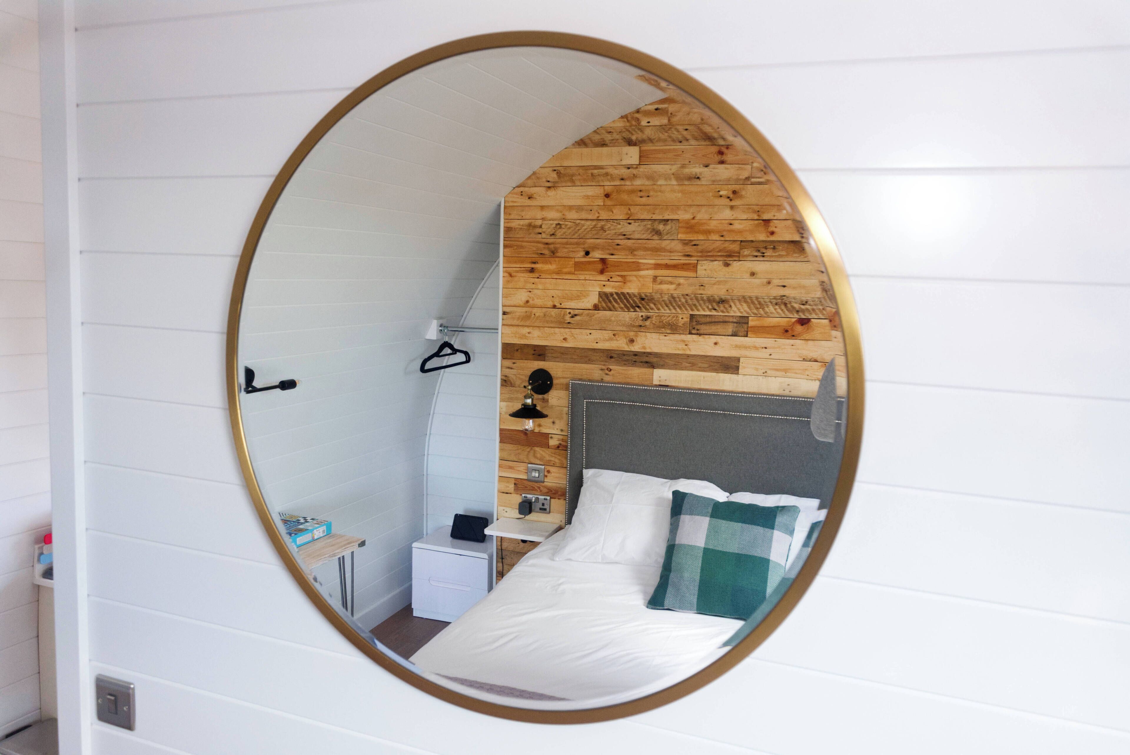 Un dormitorio con un espejo circular, un cabecero de madera, una mesita de noche y una pequeña estantería.