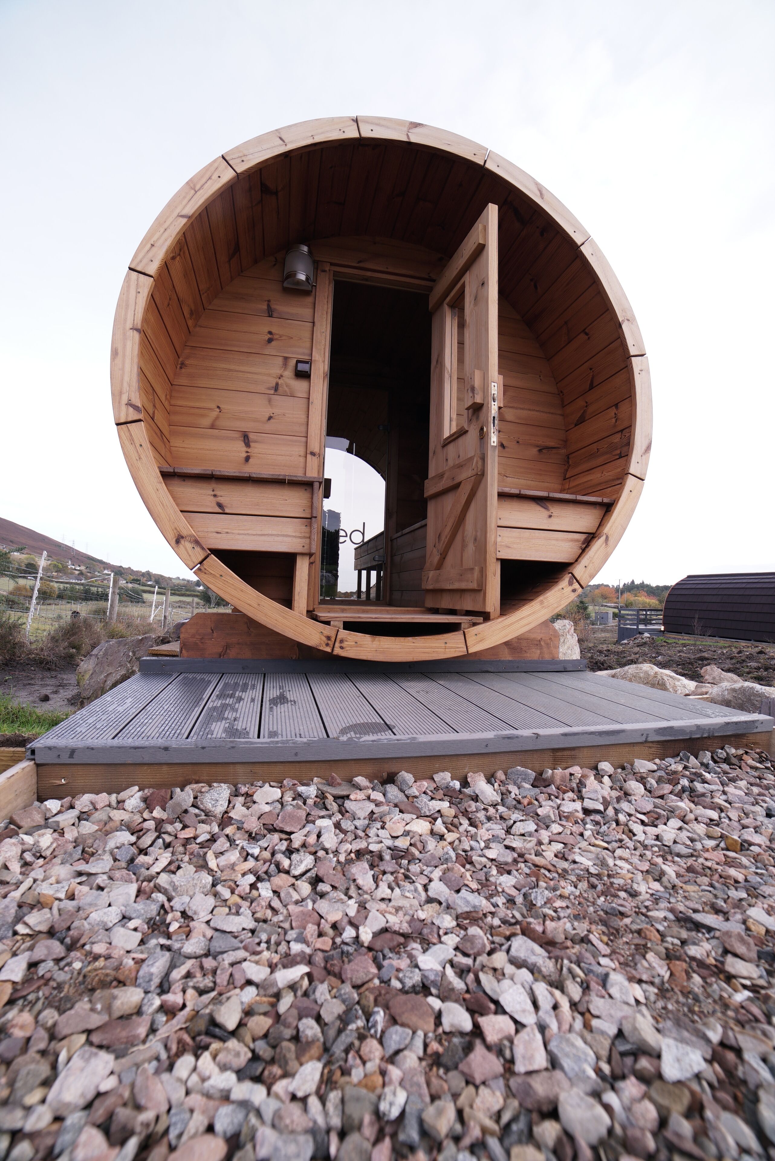 A wooden cylindrical structure with a door open, revealing a bench inside.
