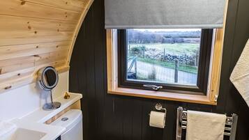 Un baño pequeño y curvo con techo de madera, ventana con vistas, inodoro, lavabo y toallero.