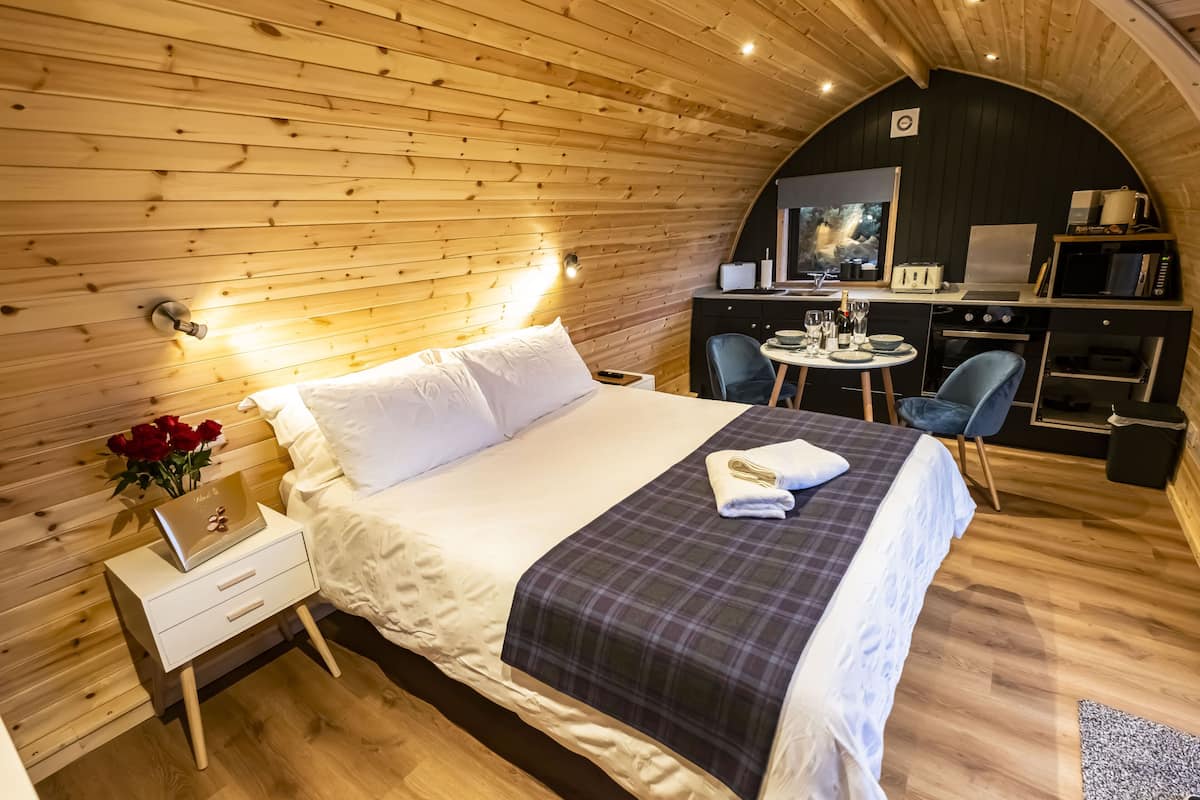 A cozy bedroom with a bed, bedside table, and a small desk area with a chair and a table.