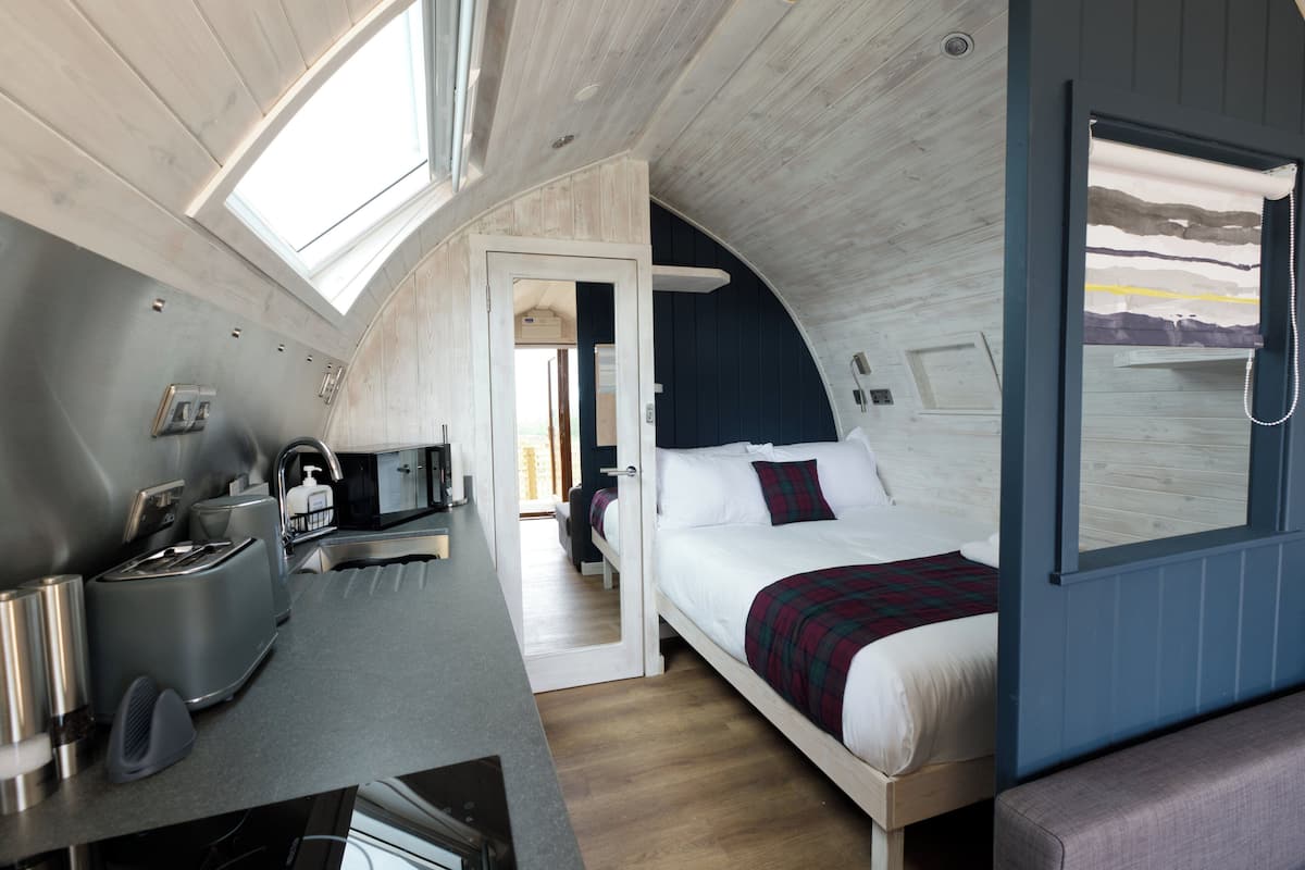 A compact, modern room with a bed, a small kitchenette, and a window providing natural light.