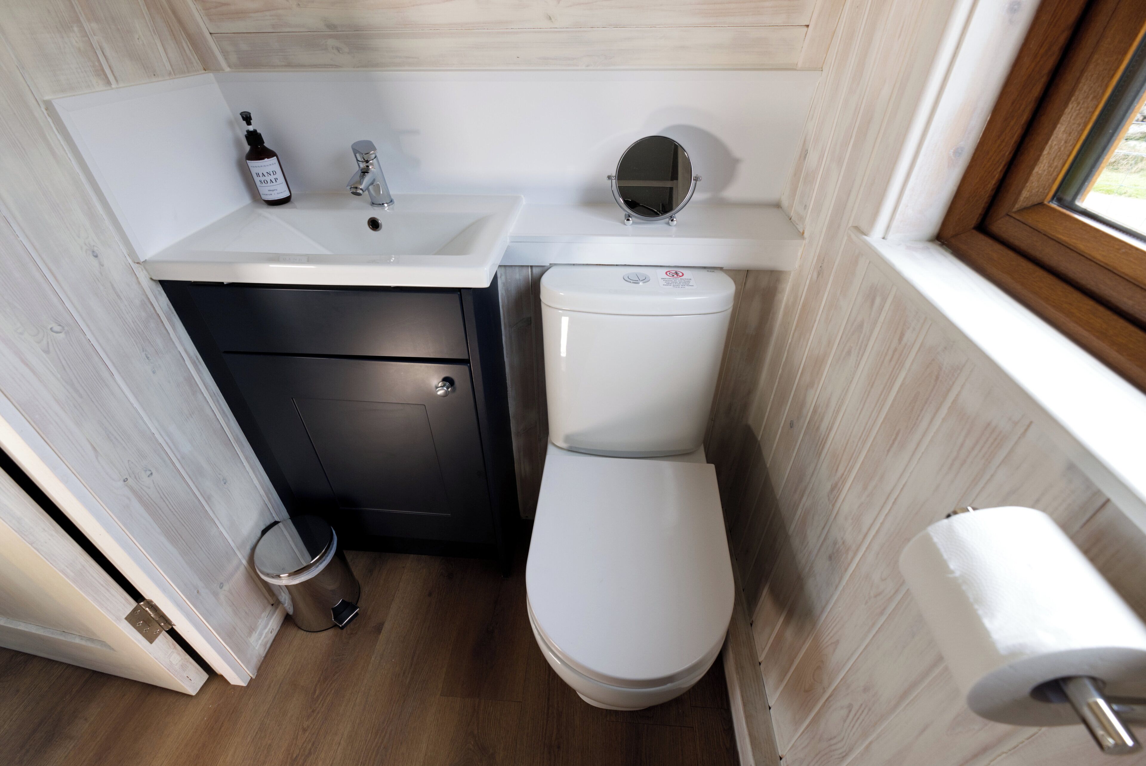 A compact bathroom with a white sink, a toilet, and a small trash bin.