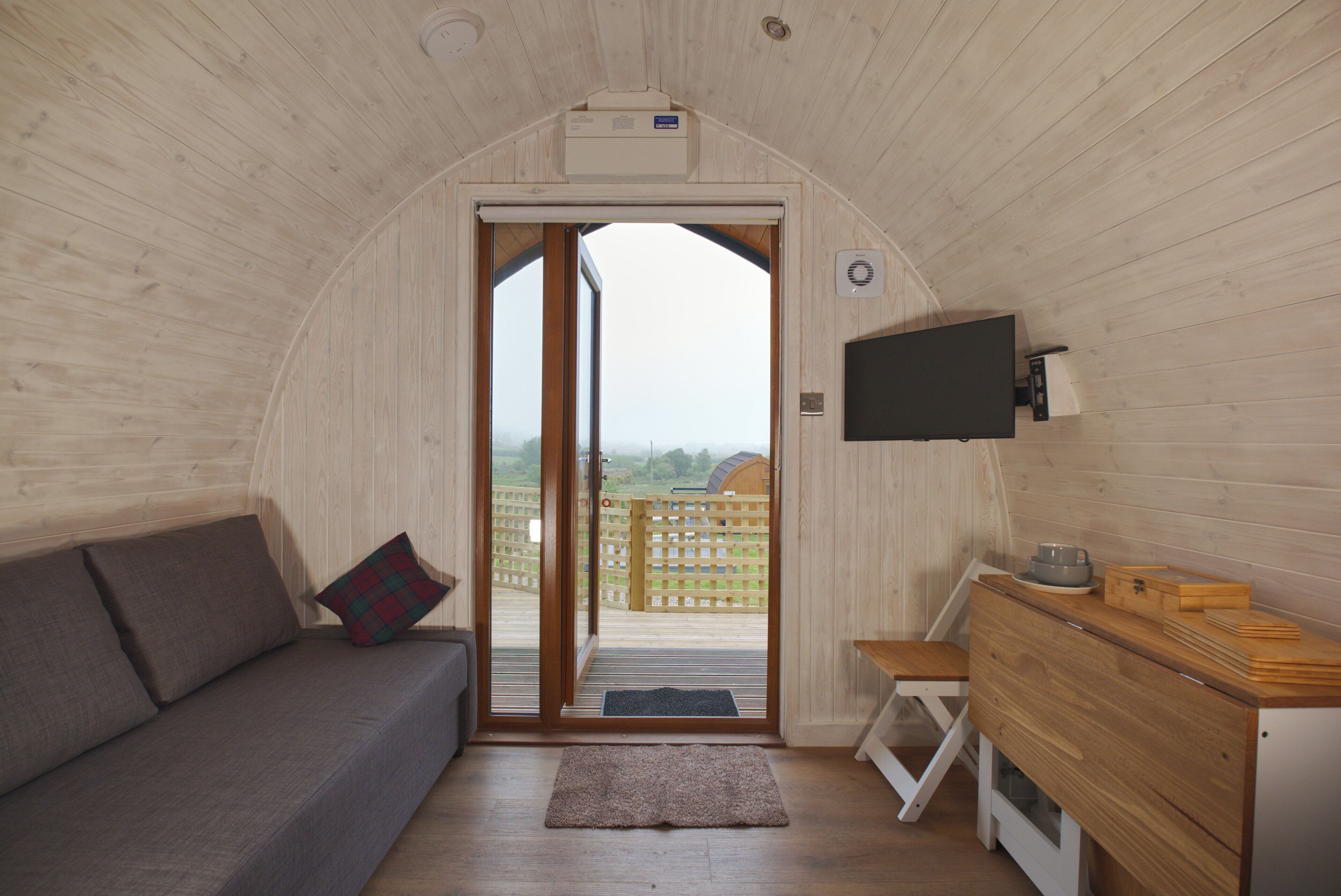 A cozy cabin interior with a sofa, a small wooden table, and a television mounted on the wall.
