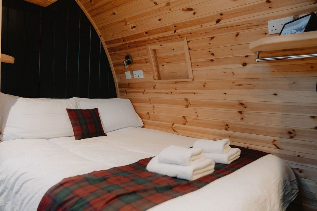 Une pièce chaleureuse aux murs en bois, avec un lit, une couverture à carreaux rouges et des serviettes soigneusement pliées.