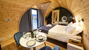 Una habitación redonda y acogedora de madera, con una cama, una mesa para dos personas y un televisor.