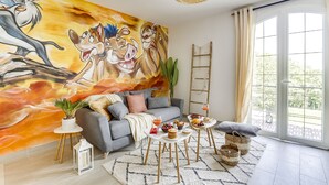 A living room with a large mural, a grey sofa, a coffee table with snacks, and a large window. - Lion King Suite - 4P near Disneyland Paris (Montry)