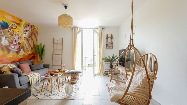A living room with a sofa, a hanging chair, a coffee table, and a large painting on the wall. - Lion King Suite - 4P near Disneyland Paris (Montry)