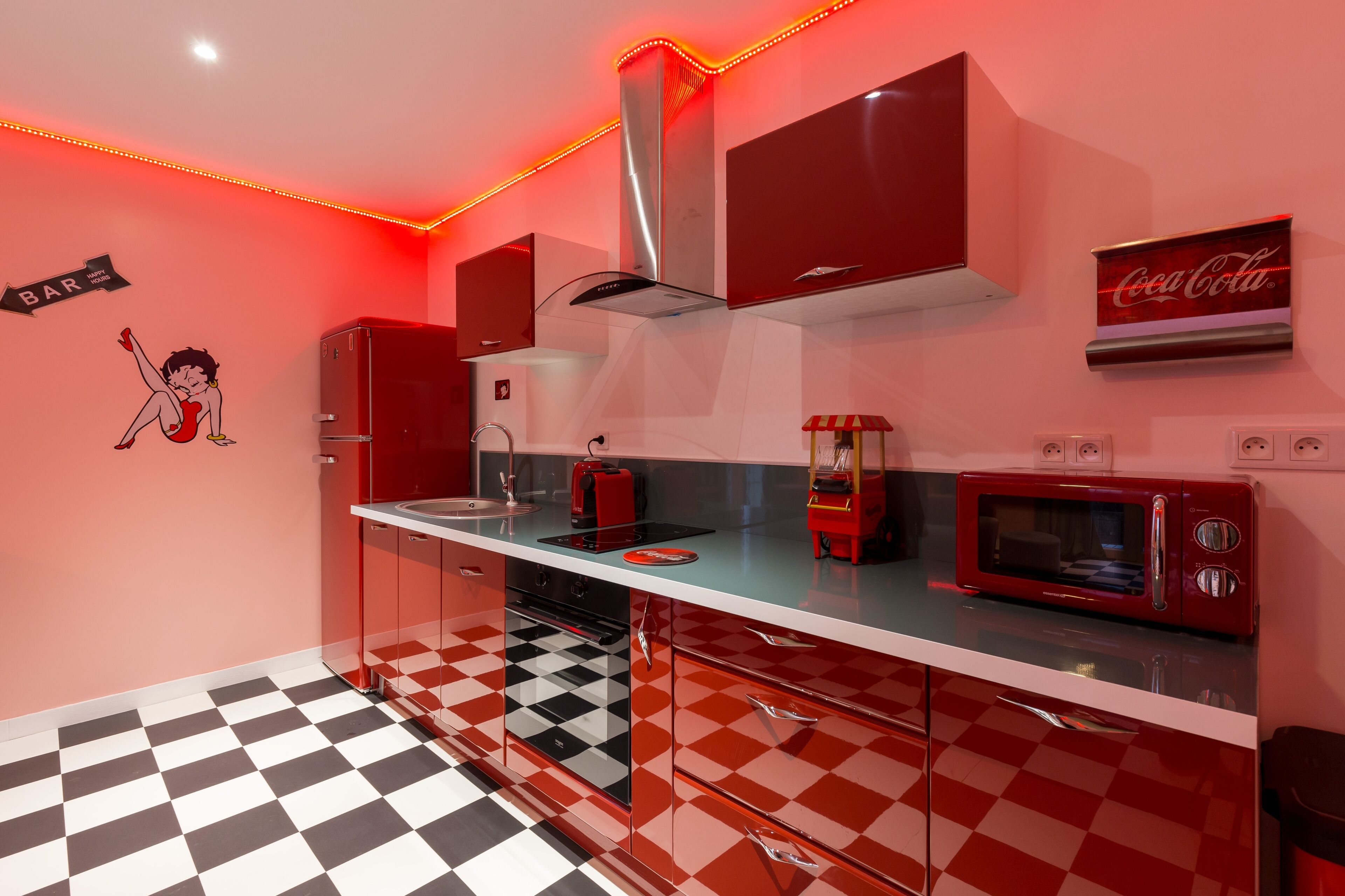 A retro-styled kitchen with a checkered floor, red cabinets, a microwave, and a Coca-Cola sign.