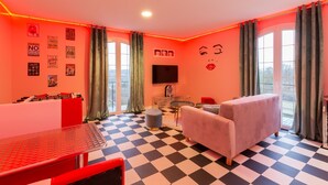 A room with a checkered floor, a sofa, a table, and a TV mounted on the wall. - Marilyn Monroe Suite - 4P with Private Jacuzzi (Montry)