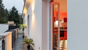 A narrow outdoor corridor with potted plants and a lantern, leading to a glass door entrance to a modern kitchen with red cabinets and a checkered floor. - Marilyn Monroe Suite - 4P with Private Jacuzzi (Montry)