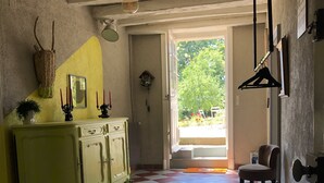Une pièce avec un sol à carreaux, une armoire jaune, un luminaire suspendu et une porte donnant sur l’extérieur.