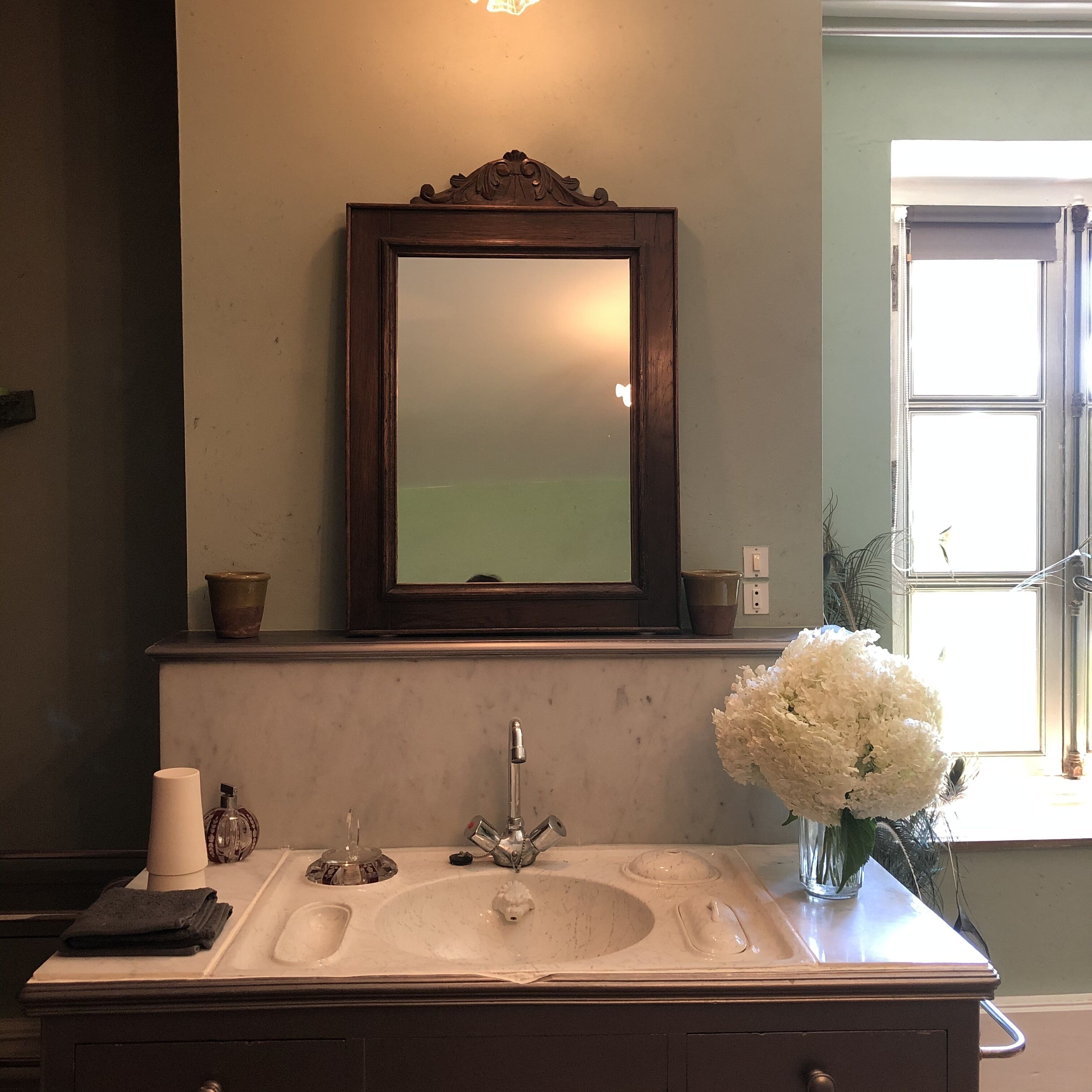 A bathroom with a large mirror, a sink with a faucet, and a vase with white flowers.