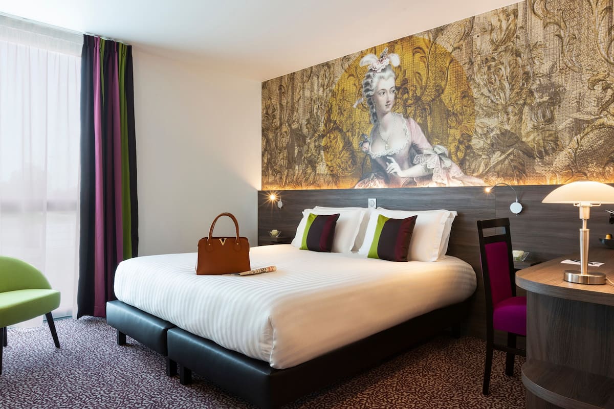 Une chambre d’hôtel avec un grand lit, une table de chevet, une chaise, une lampe et un tableau au mur.