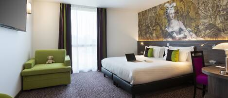 Quarto de hotel com cama, escrivaninha, cadeira e uma tapeçaria grande na parede.