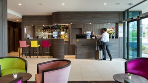 Un moderno vestíbulo de hotel con una recepción, una zona de bar y asientos coloridos.