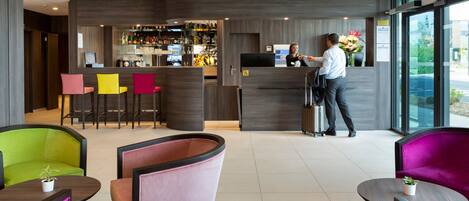 A modern hotel lobby with a reception desk, bar area, and colorful seating.