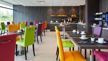 Un comedor moderno con sillas y mesas coloridas, una encimera de cocina con alimentos y una máquina de café.
