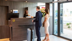 Mostrador de recepción con pantalla digital, señal de accesibilidad para sillas de ruedas y ventana con vistas al exterior.