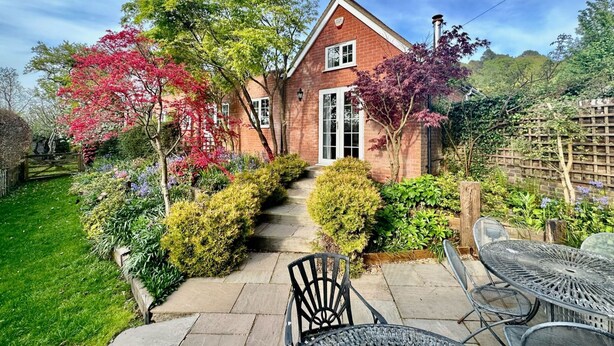 A brick house with a front garden, a paved pathway leading to the entrance, and outdoor furniture. - New Forest Cottages. (Godshill)