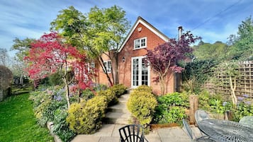 A brick house with a front garden, a paved pathway leading to the entrance, and outdoor furniture.