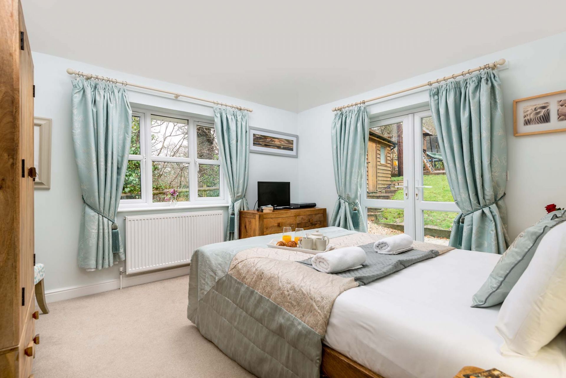 A bedroom with a bed, a dresser, a TV, and windows with curtains.