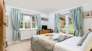 A bedroom with a bed, a dresser, a TV, and windows with curtains. - New Forest Cottages. (Godshill)