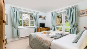 A bedroom with a bed, a dresser, a TV, and windows with curtains.