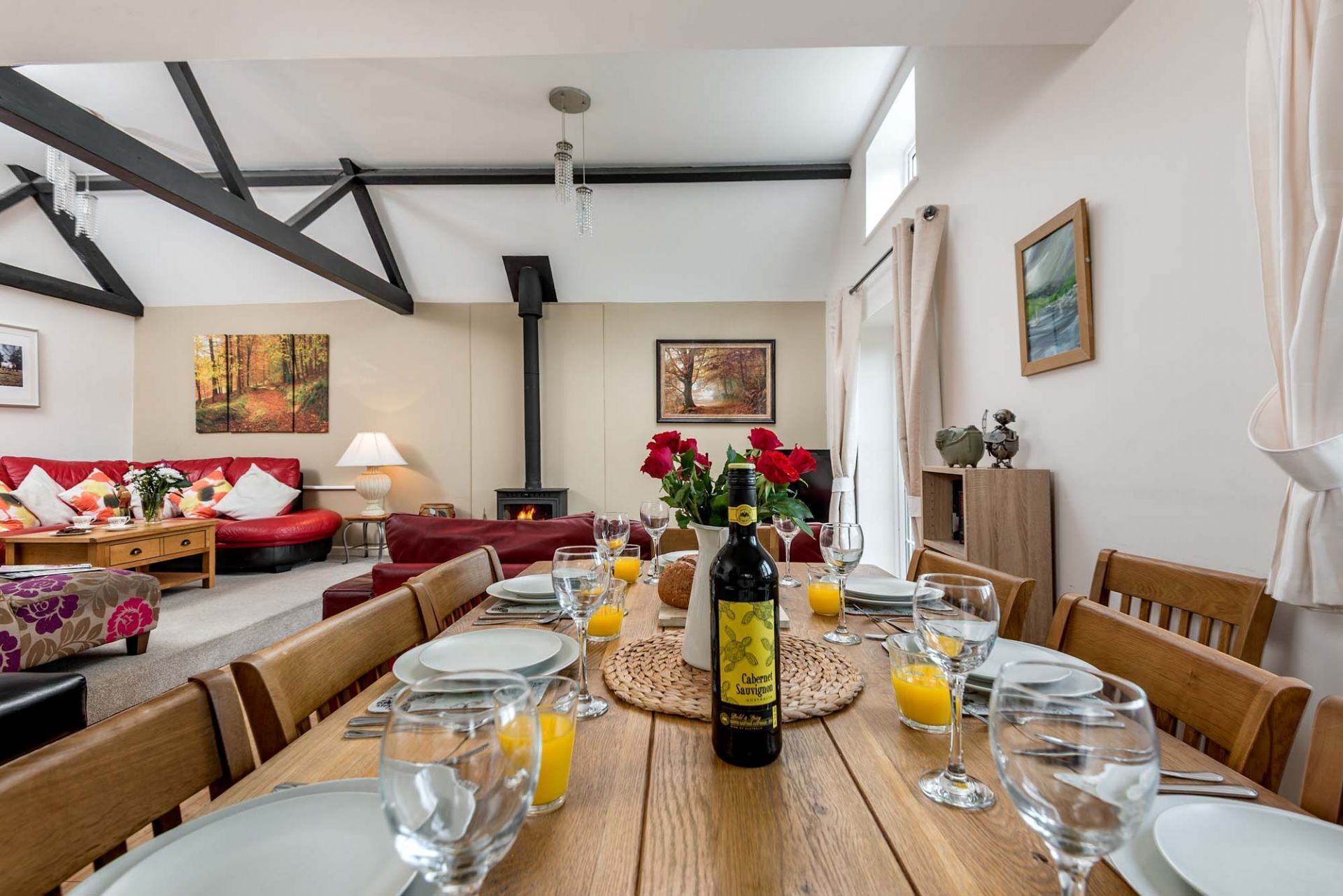 A dining area with a wooden table set for a meal, a bottle of wine, and a fireplace in the background.