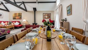 A dining area with a wooden table set for a meal, a bottle of wine, and a fireplace in the background. - New Forest Cottages. (Godshill)