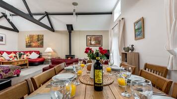 A dining area with a wooden table set for a meal, a bottle of wine, and a fireplace in the background.