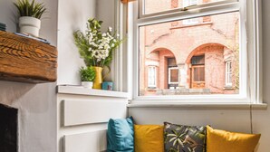 A cozy seating area with a blue bench, yellow and blue cushions, and a window offering a view of a red brick building. - Stonesthrow Townhouse (Leek)