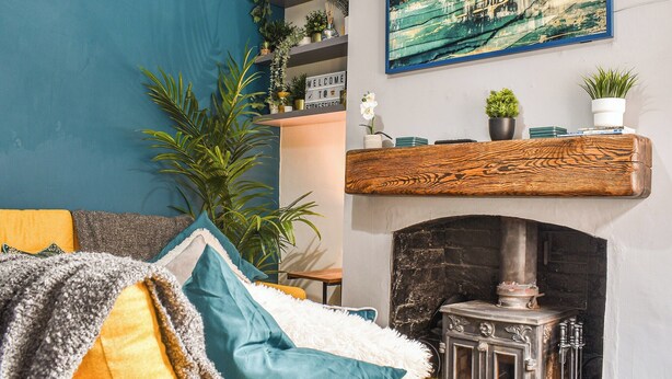 A cozy living room with a fireplace, a blue accent wall, and a variety of plants and books. - Stonesthrow Townhouse (Leek)