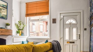 A room with a yellow sofa, a window with blinds, a door with a sign, and a small table. - Stonesthrow Townhouse (Leek)