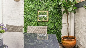 A patio with a green wall, a welcome sign, a wicker chair, and a potted plant. - Stonesthrow Townhouse (Leek)