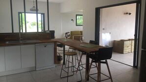 Een moderne keuken met een houten aanrecht, barstoelen en een eettafel. Er is een raam dat natuurlijk licht en uitzicht op groen biedt.