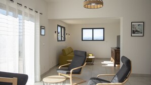 Een ruime zithoek met een moderne bank, twee fauteuils, een klein rond tafeltje en een houten kast.