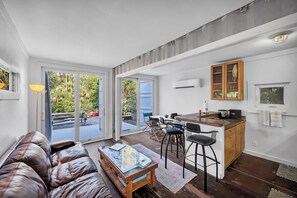 A modern living space with a leather sofa, wooden coffee table, and a kitchen area with bar stools.