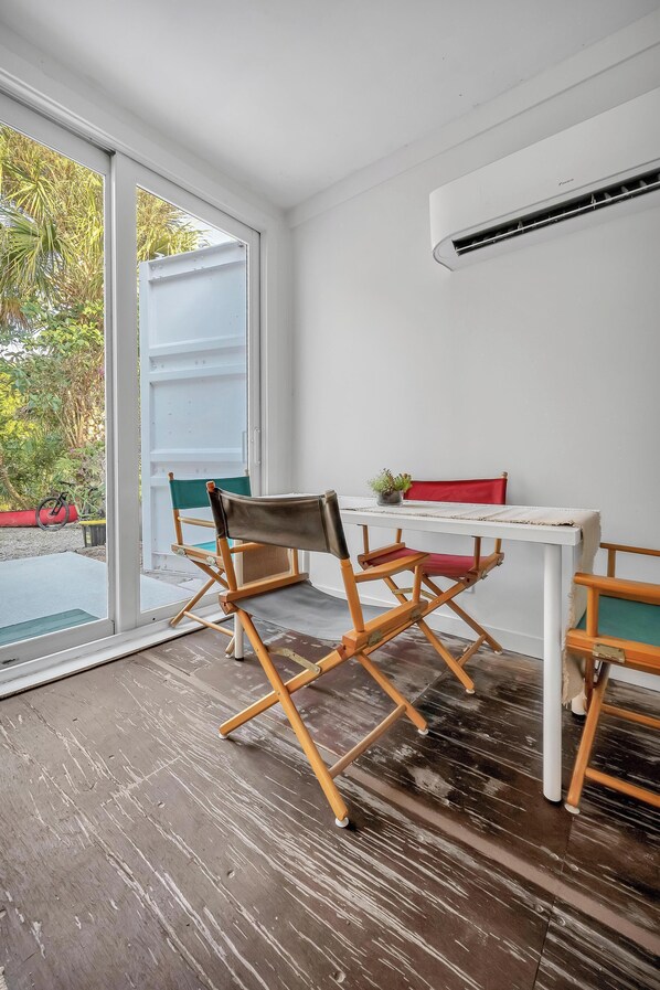 A room with a white table, director's chairs, a potted plant, and an air conditioning unit.