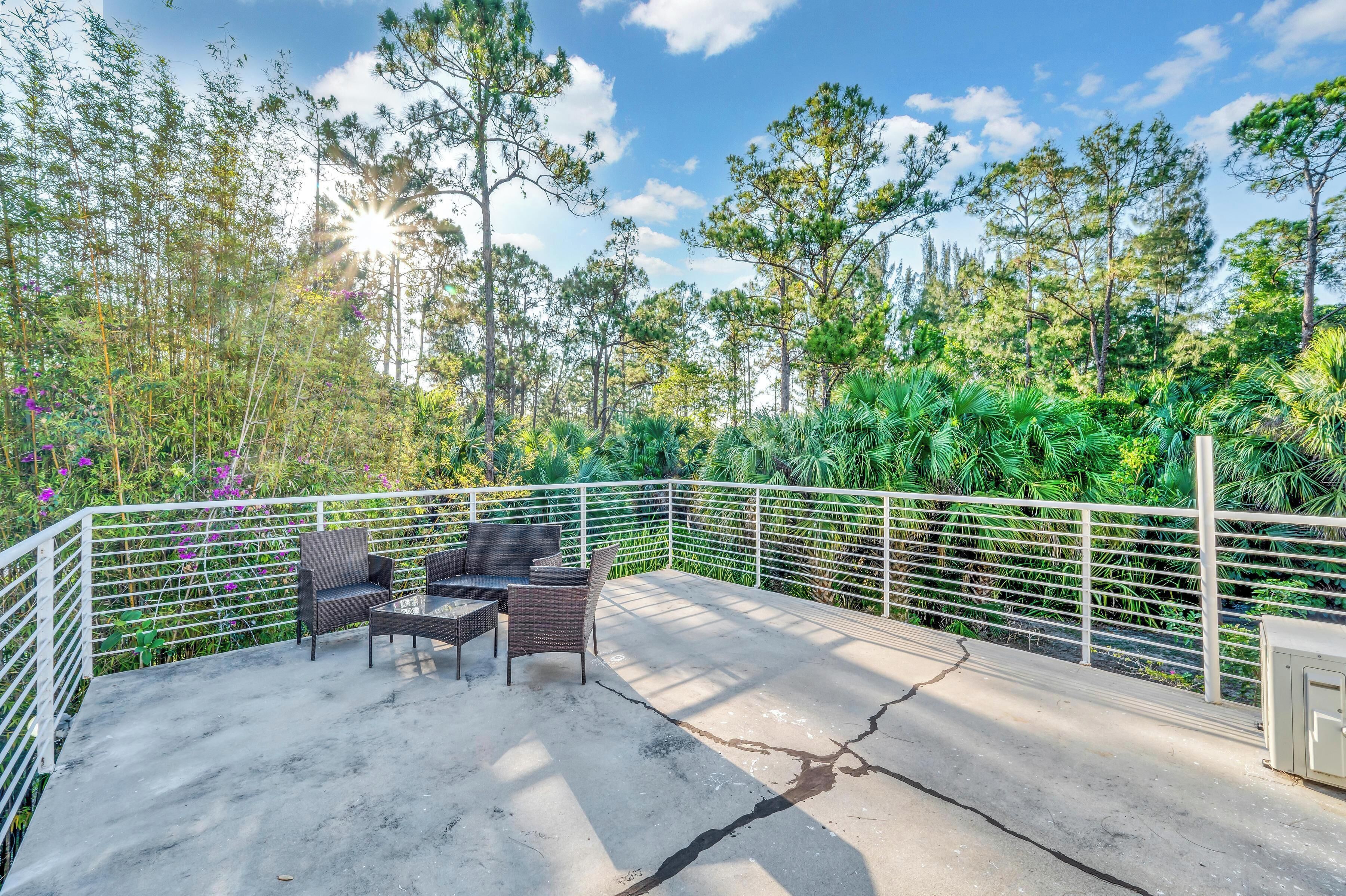 An outdoor patio area with a concrete floor, white metal railing, and wicker furniture.