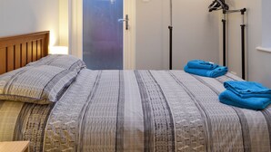 A bedroom with a bed, a door, a towel rack, and a painting on the wall. - 3 bedroom accommodation in Sheringham (Sheringham)