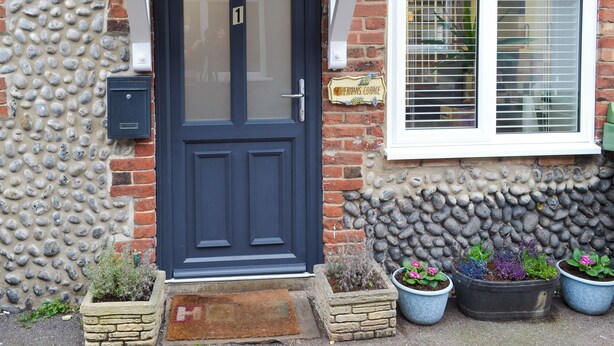 A house with a dark blue door, a brick exterior, and a window with blinds. There are potted plants in front of the house. - 3 bedroom accommodation in Sheringham (Sheringham)