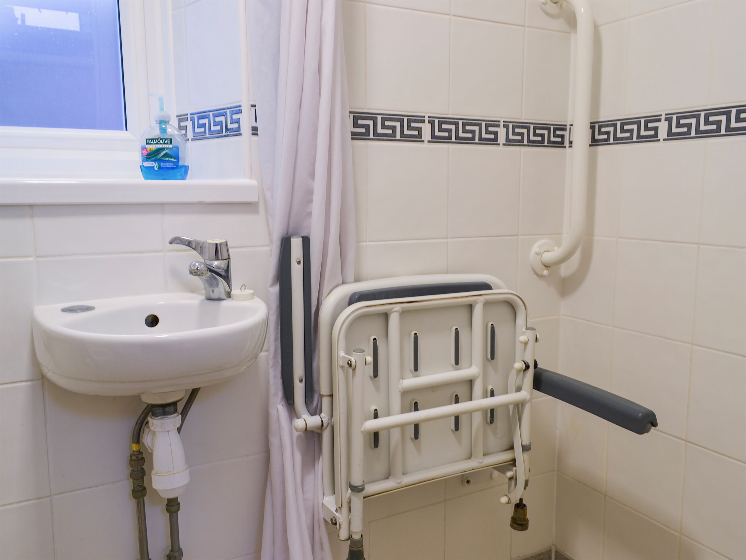 A bathroom with a white sink, a shower curtain, and a grab bar.