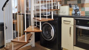 A compact kitchen with a built-in washer and dryer, a small oven, and a staircase with a metal railing. - 3 bedroom accommodation in Sheringham (Sheringham)