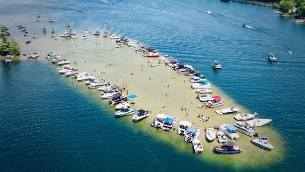 Vue aérienne d’une marina où de nombreux bateaux sont amarrés le long d’une plage étroite et sablonneuse.