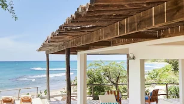 A covered outdoor area with a pool, lounge chairs, and a view of the ocean.