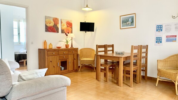 A living room with a sofa, a dining table with chairs, a TV, and artwork on the walls.