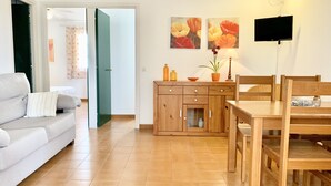 Una sala de estar con un sofá, una mesa de comedor de madera y un televisor. Hay cuadros en la pared y una planta sobre la mesa.