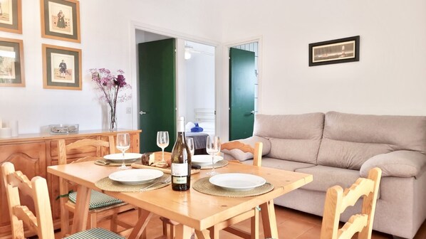 A dining area with a wooden table set for two, a bottle of wine, and a green door in the background.